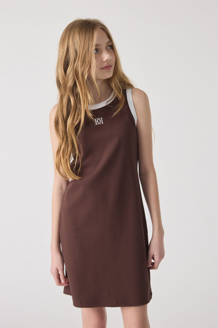 Girl wearing a sleeveless chocolate brown monogram dress with white trim, styled in a simple, effortless look.