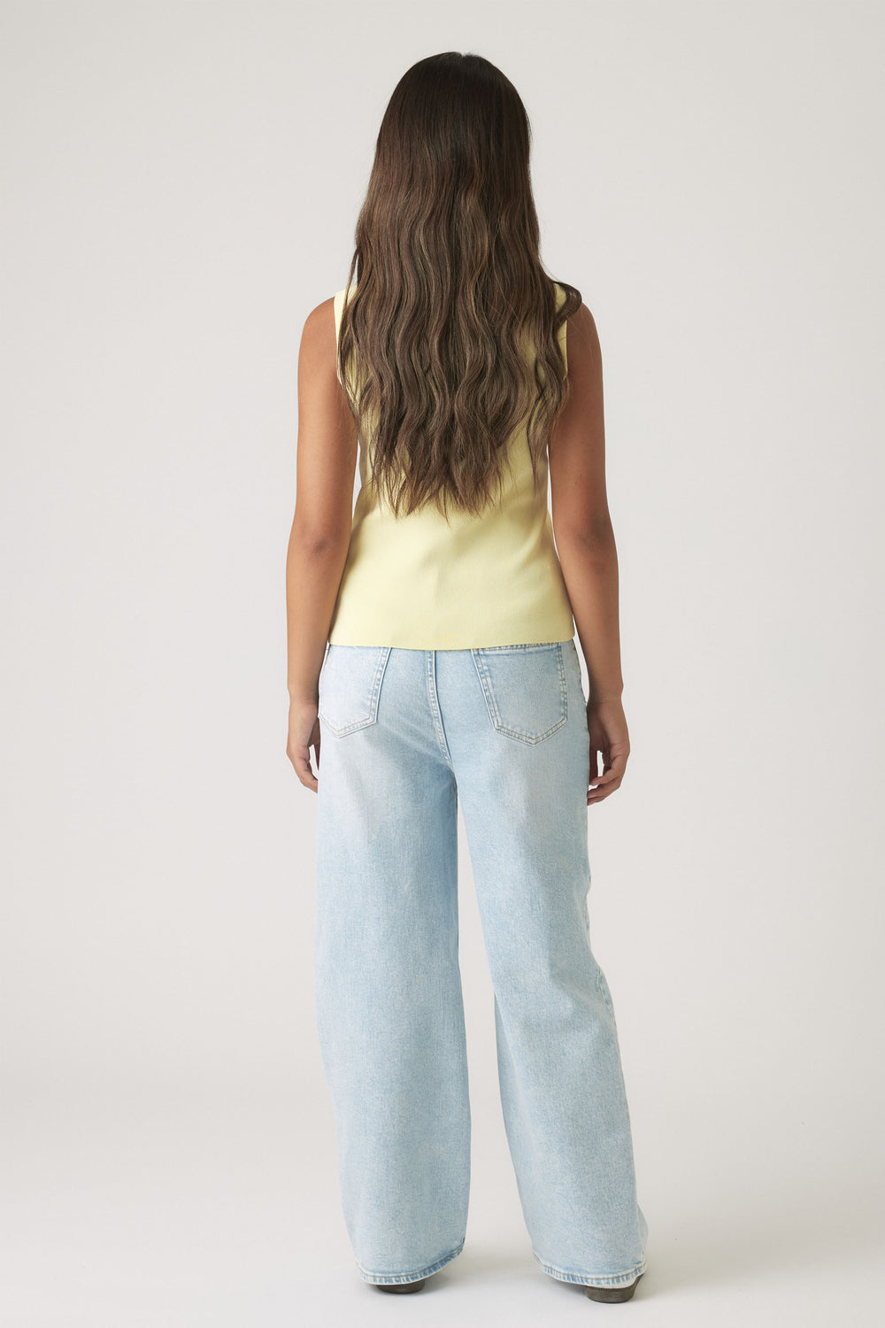 Girl shown from behind wearing a buttercup yellow sleeveless knit vest paired with light blue wide-leg jeans