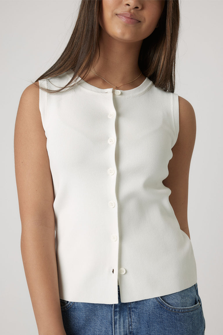 Cream sleeveless knit vest with front buttons, styled casually with blue denim jeans for an easy everyday look.