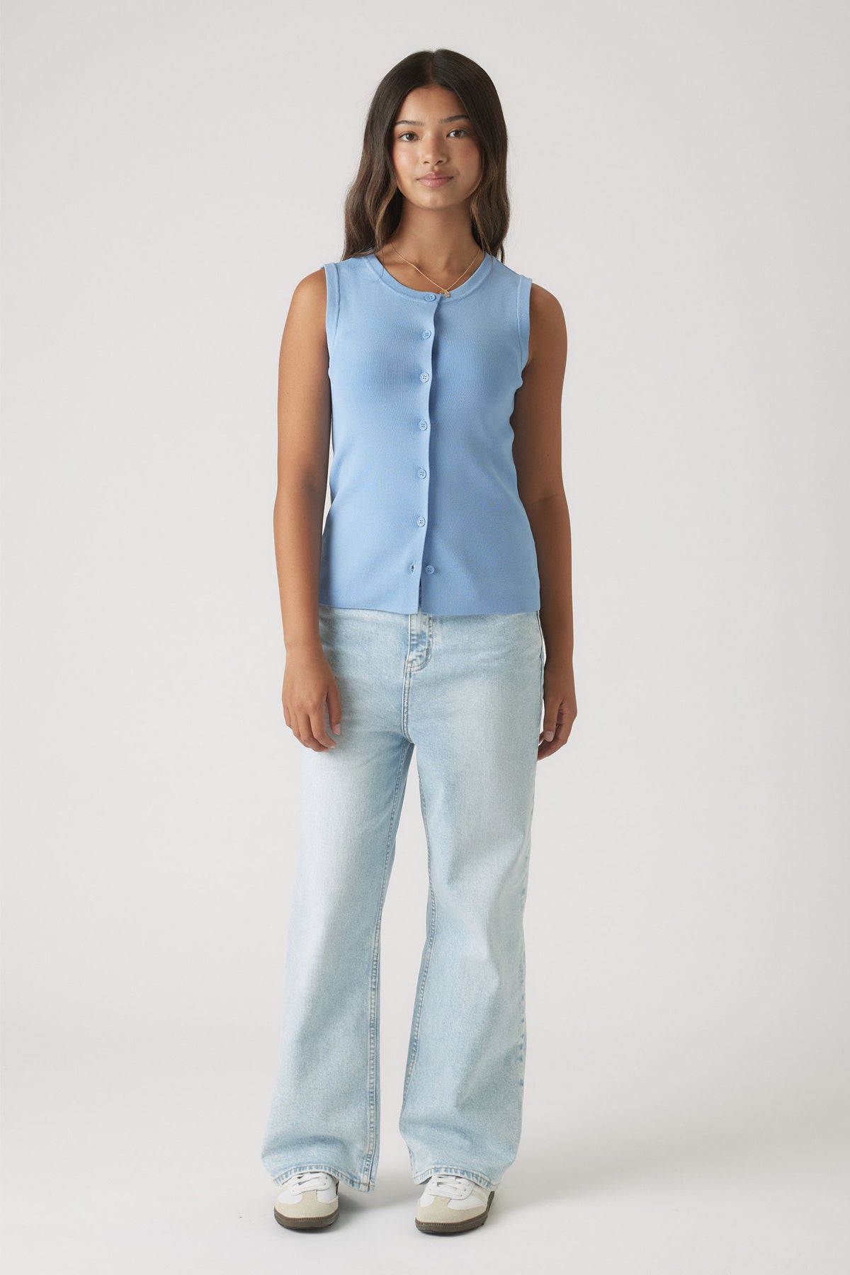 Teen girl wearing a soft dusty blue sleeveless knit vest paired with light wash wide-leg denim jeans and sneakers