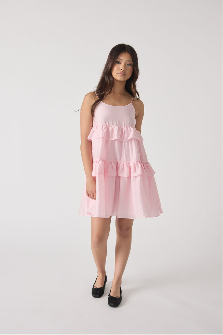 Girl wearing a soft pink sleeveless dress with tiered ruffles and thin straps, paired with black ballet flats.