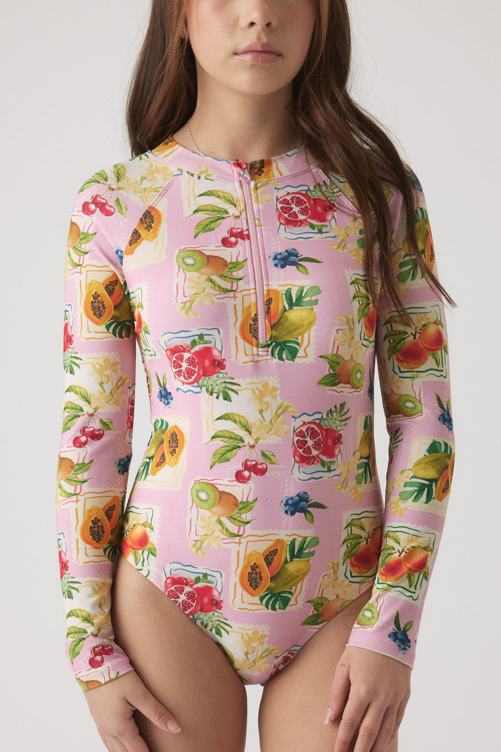 Young girl wearing a pink long sleeve swimsuit with vibrant tropical fruit prints and a front zipper detail.