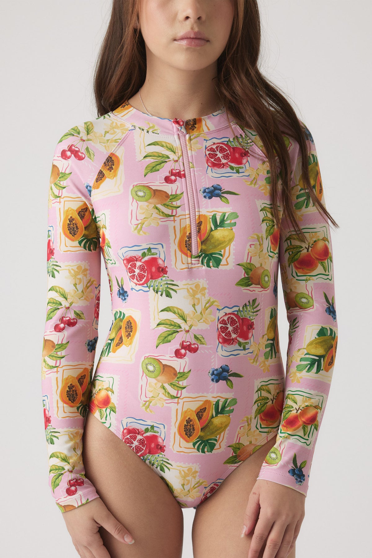 Young girl wearing a pink long sleeve swimsuit with vibrant tropical fruit prints and a front zipper detail.