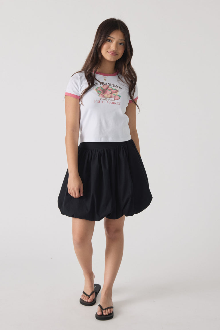 Girl wearing a white ringer tee with pink trim and graphic print, paired with a voluminous black skirt and sandals.