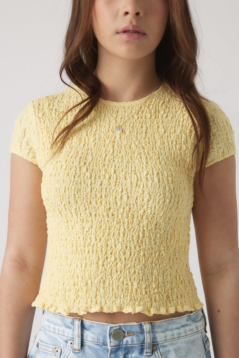 Close-up of girl wearing a soft yellow textured short sleeve top paired with light wash denim jeans.
