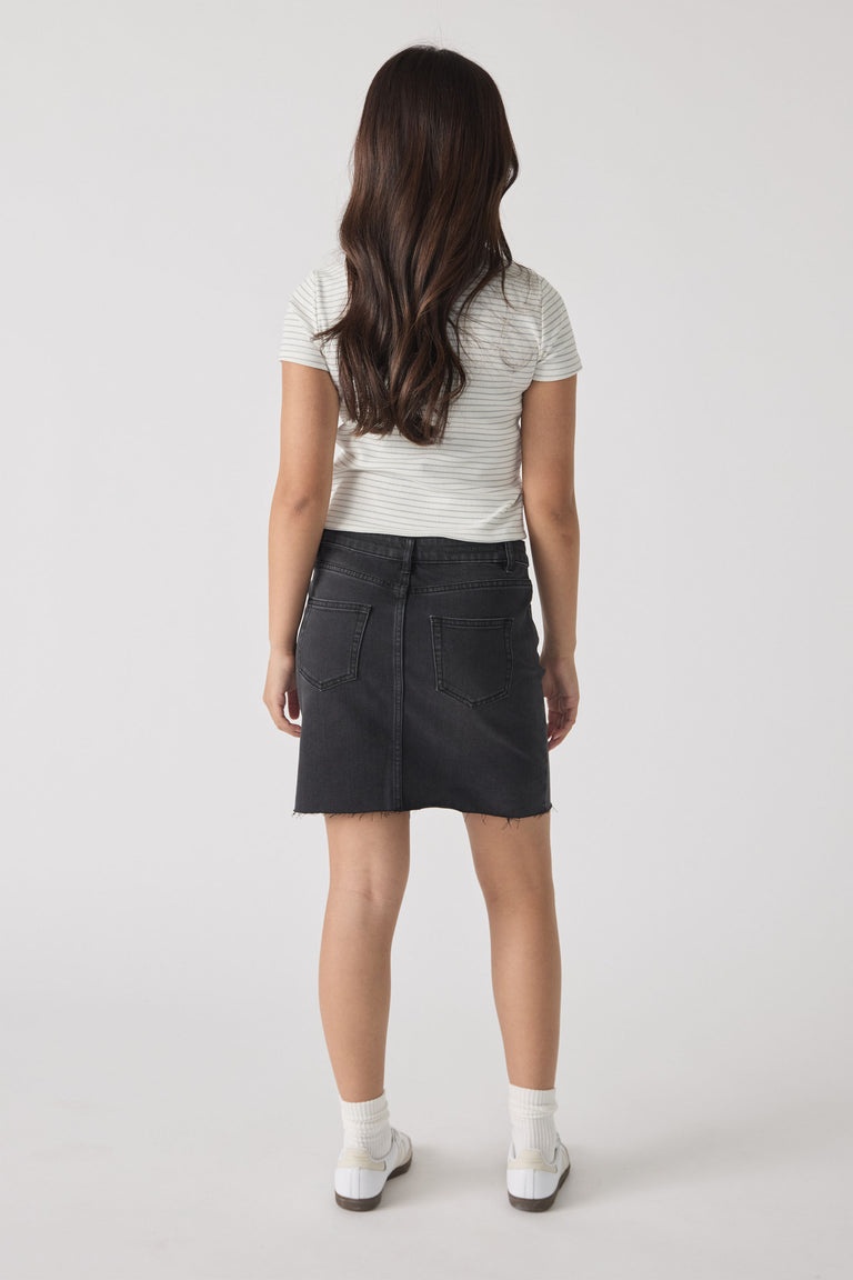 Girl wearing a short-sleeve striped tee paired with a black denim skirt and white ankle socks and sneakers, shown from behind.