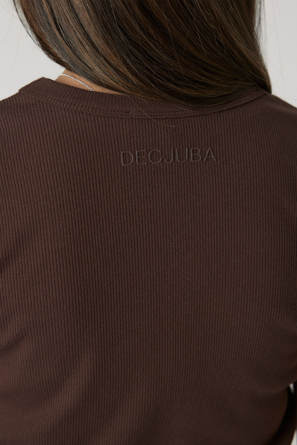 Close-up of a girl wearing a ribbed chocolate brown crop tee with subtle branded embroidery at the back neckline.