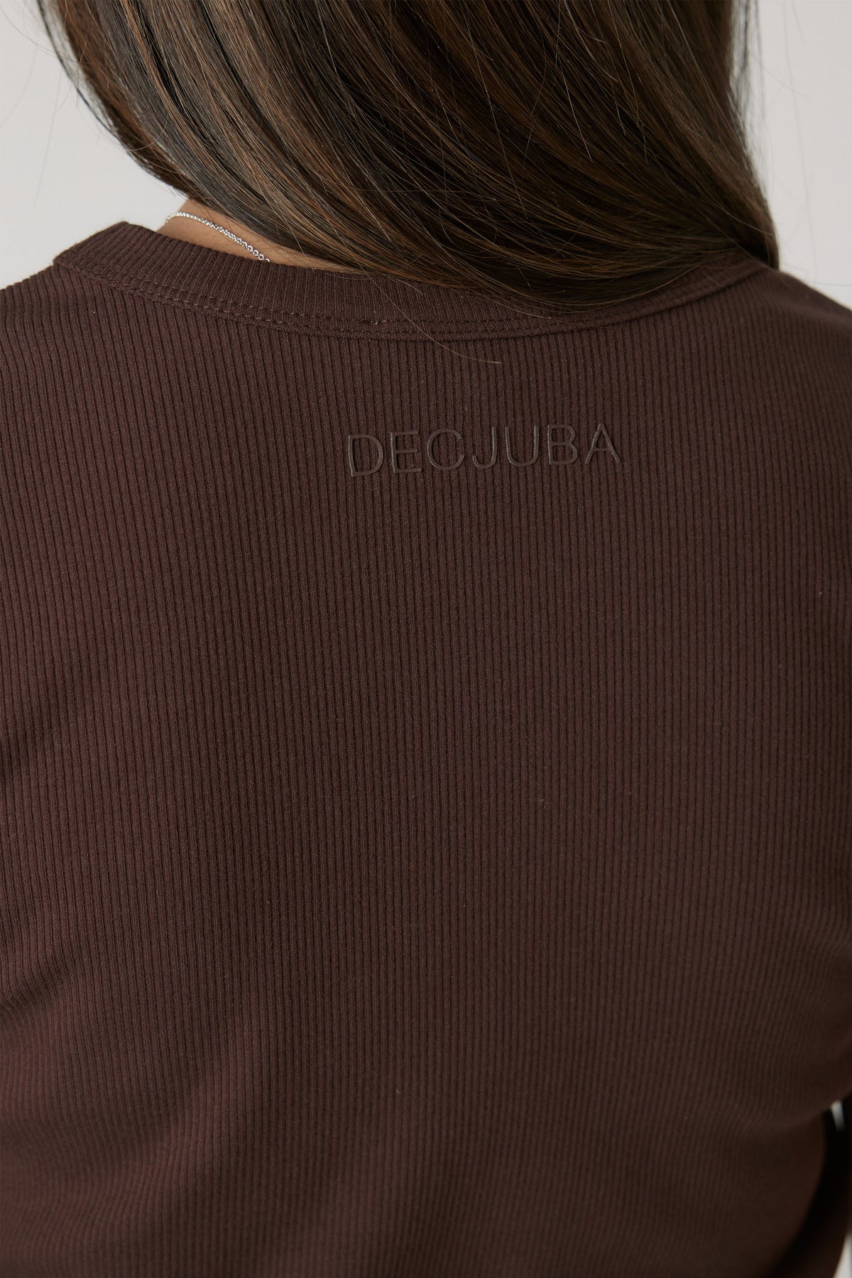 Close-up of a girl wearing a ribbed chocolate brown crop tee with subtle branded embroidery at the back neckline.
