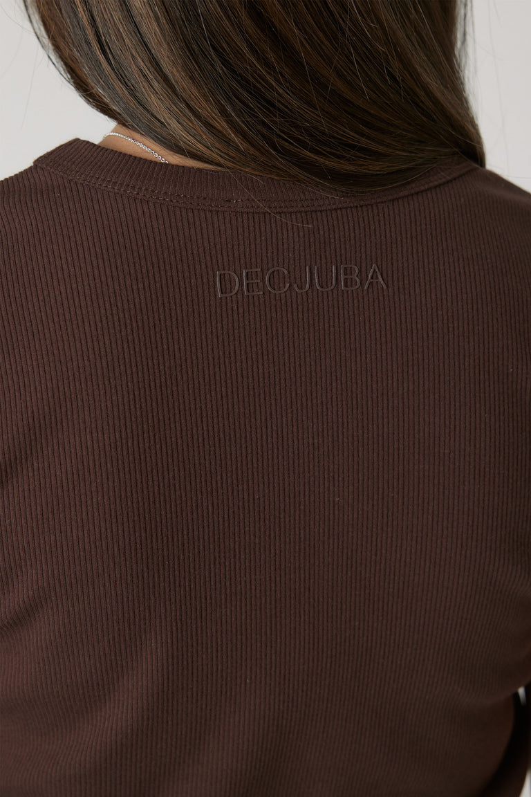 Close-up of a girl wearing a ribbed chocolate brown crop tee with subtle branded embroidery at the back neckline.