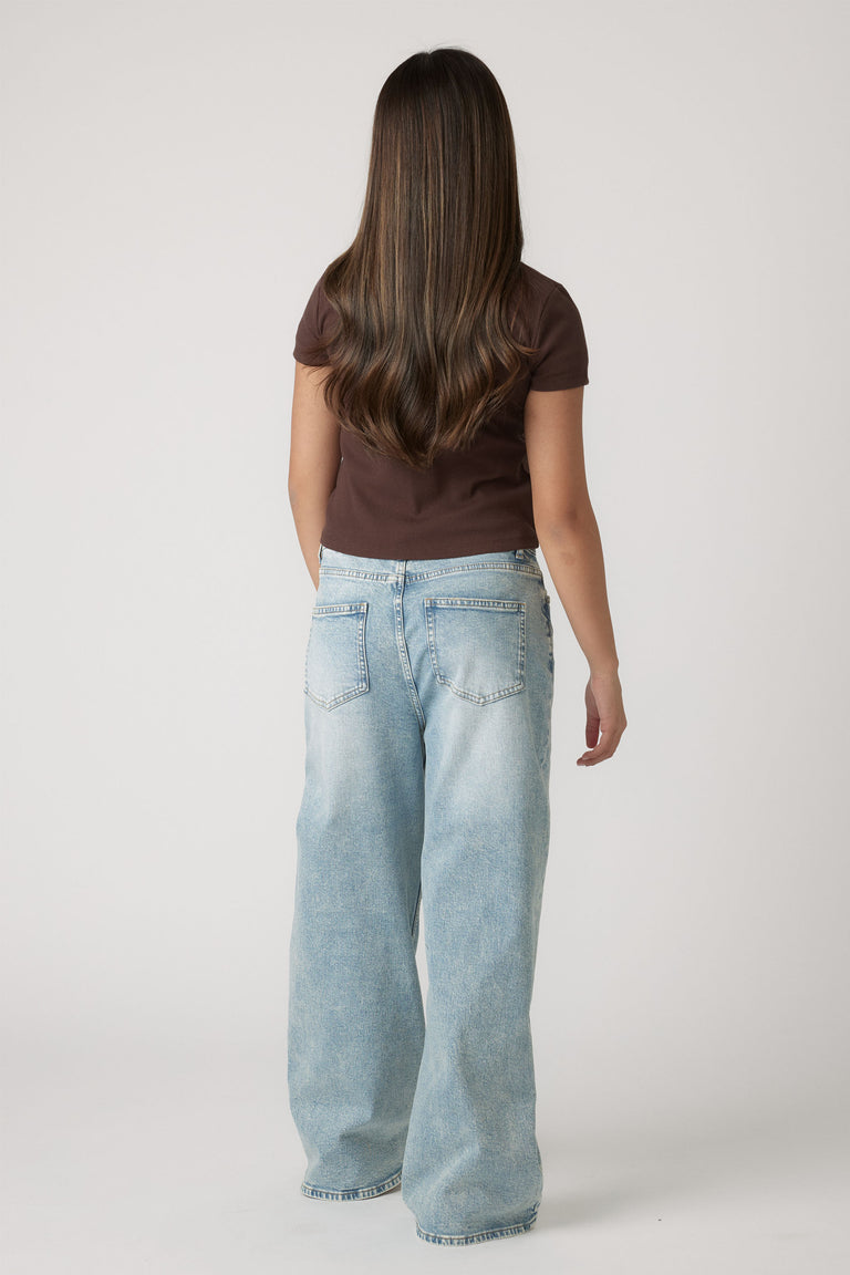 Girl wearing a chocolate brown crop tee paired with relaxed fit light blue denim jeans, shown from the back.