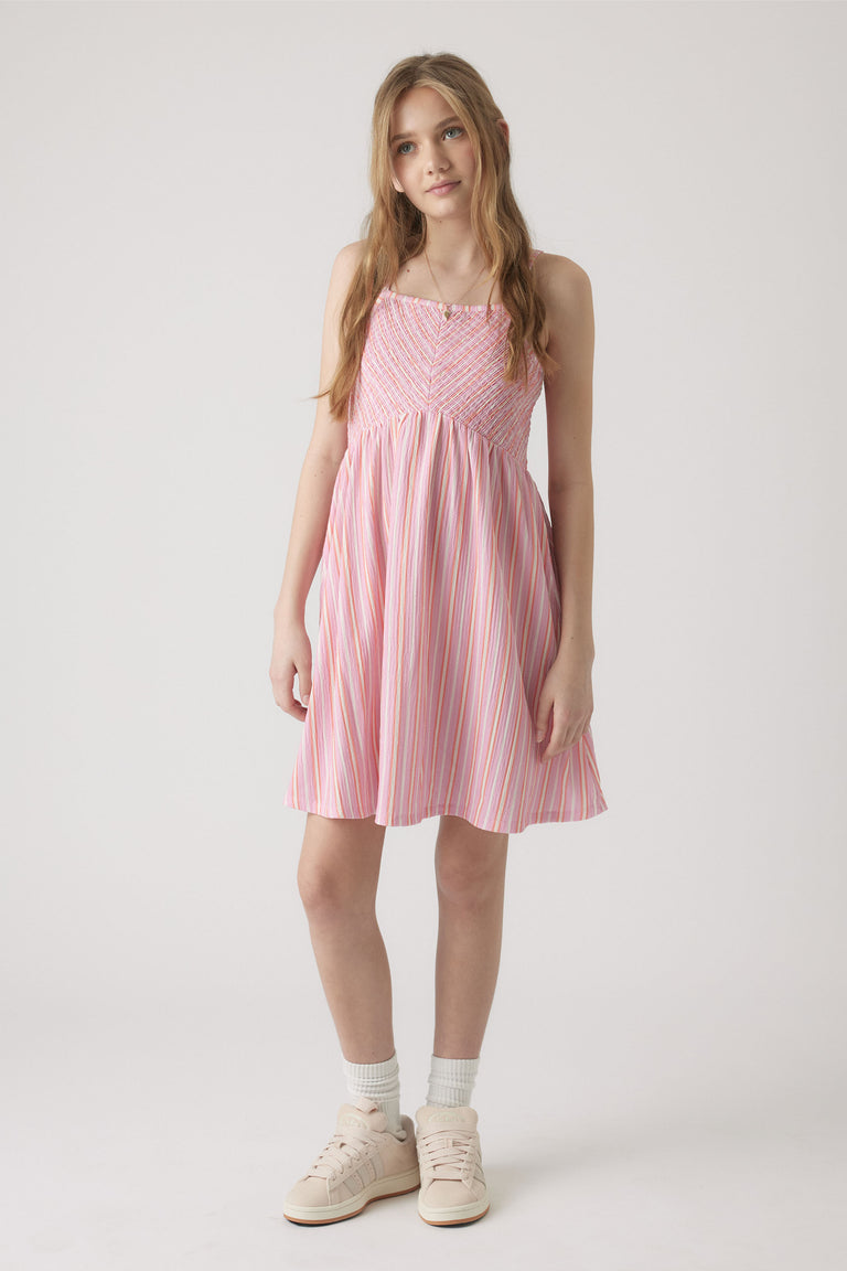 Girl wearing a pink and white striped shirred dress with spaghetti straps, paired with white socks and sneakers.