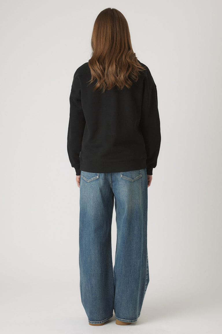 Back view of girl wearing a relaxed black oversized hoodie paired with wide-leg light blue denim jeans