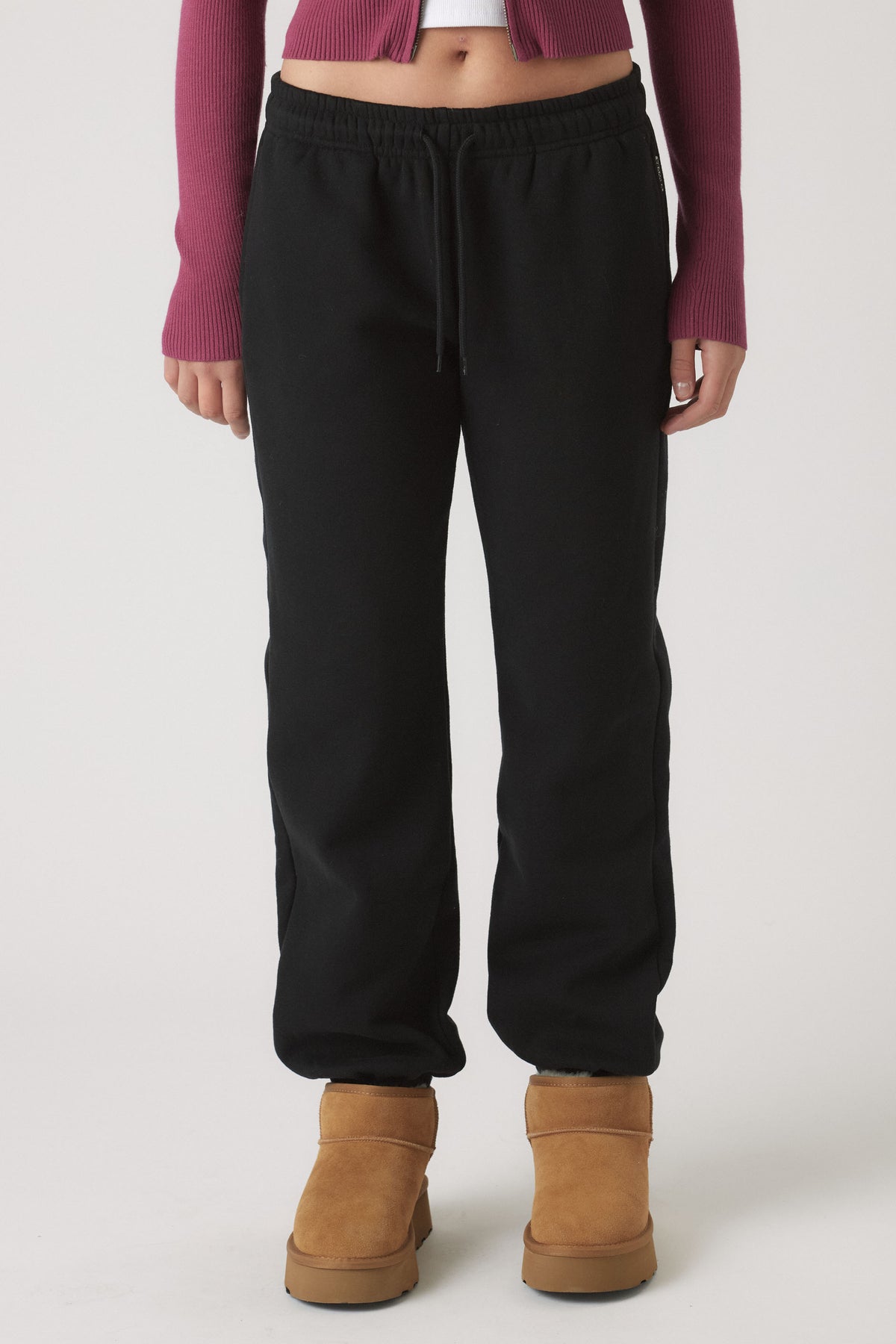 Front view of girl wearing relaxed black elastic cuff track pants paired with tan ankle boots and cropped maroon top