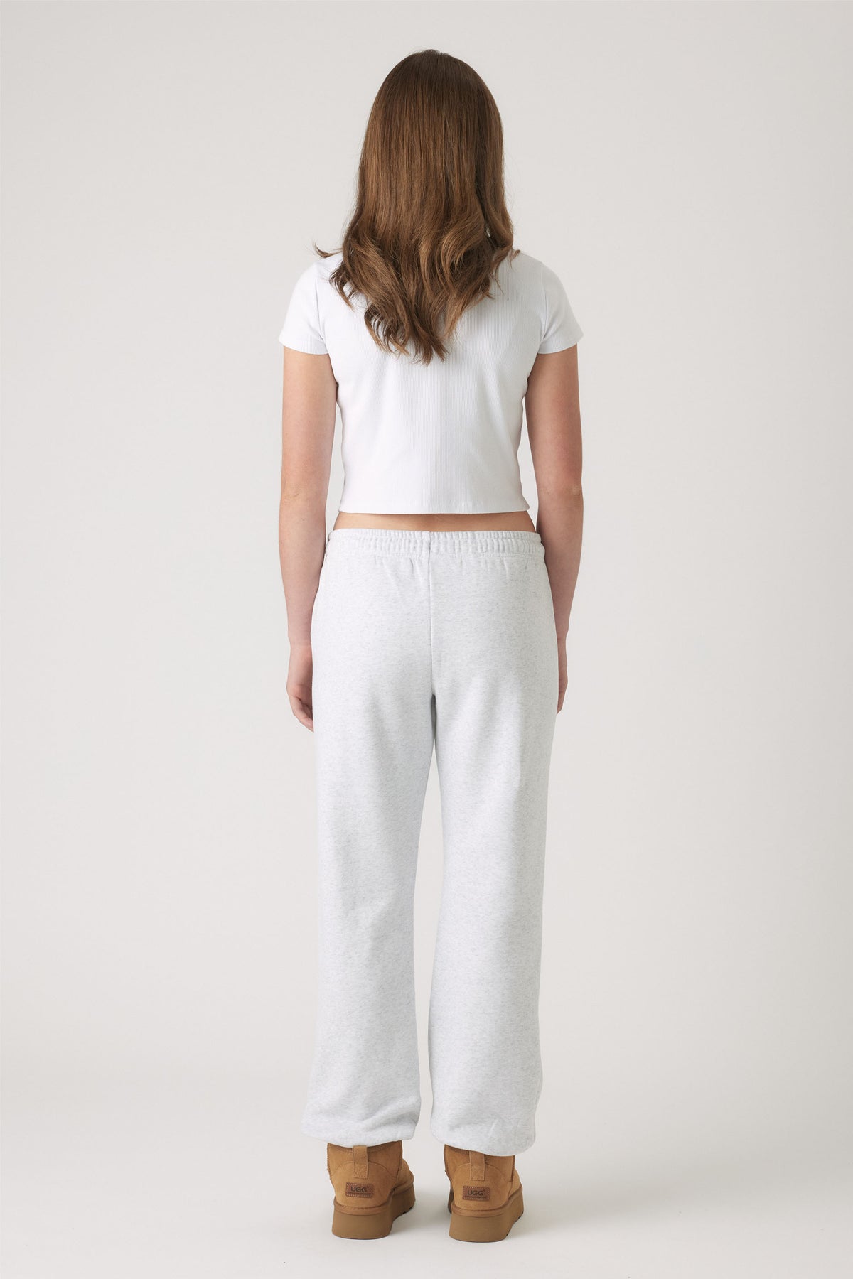 Girl wearing light grey elastic cuff track pants paired with a fitted white crop top and tan boots for casual style.