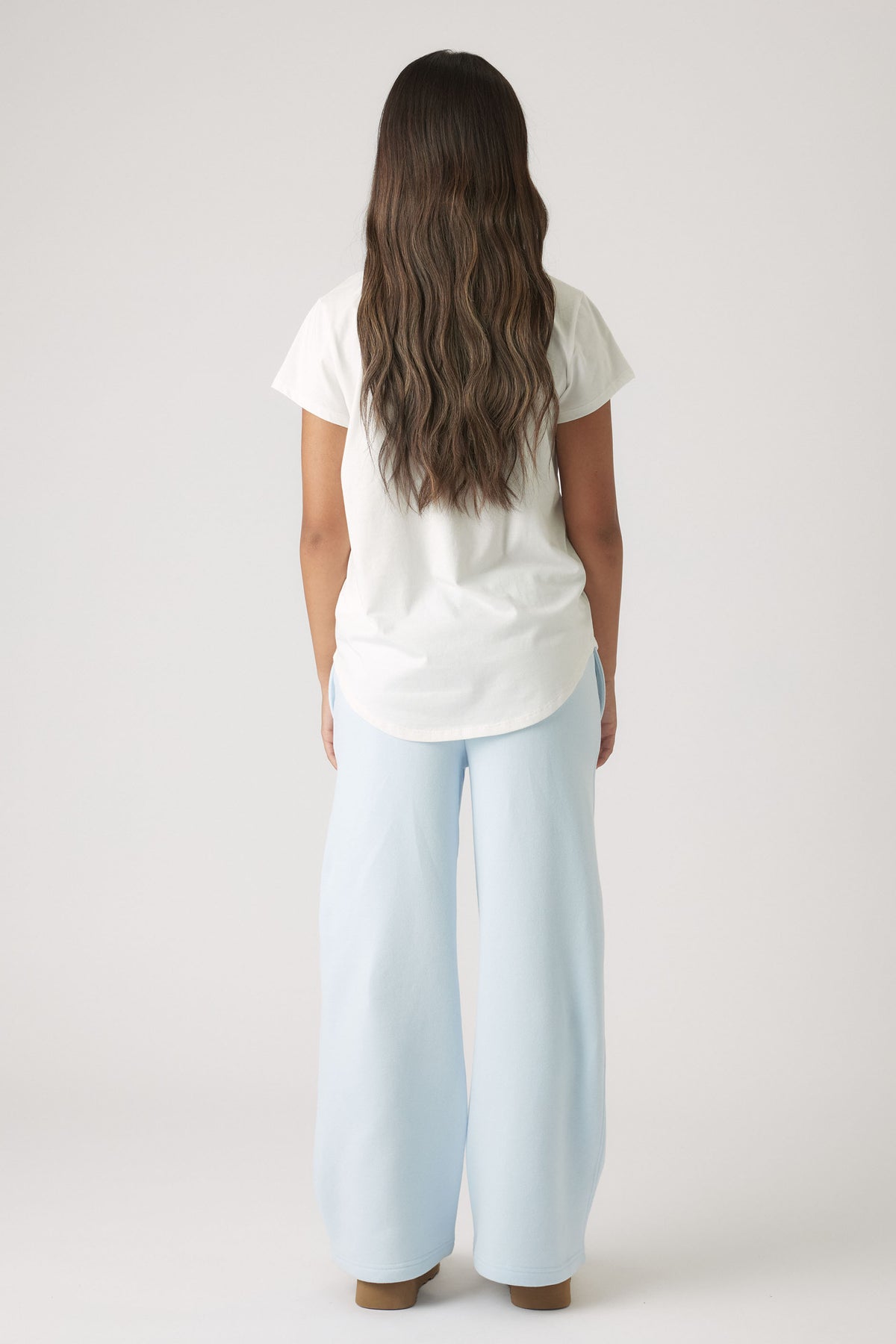 Back view of girl wearing a white embellished tee paired with relaxed light blue wide-leg pants and brown shoes