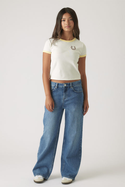 Teen girl wearing a white cropped ringer tee with yellow trim paired with relaxed wide-leg blue denim jeans and sneakers