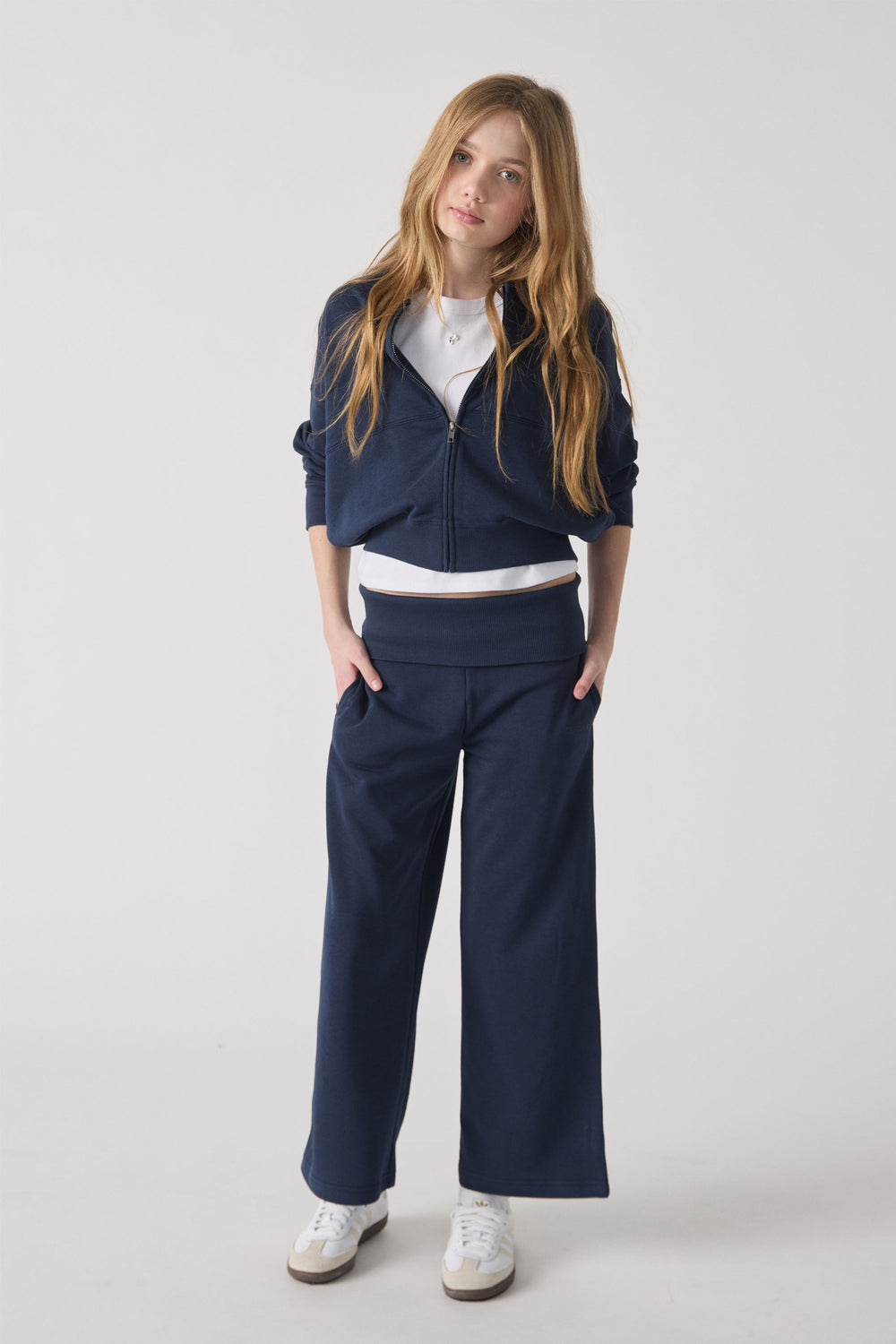 Girl wearing navy rolled waist track pants paired with a white tee and matching zip-up jacket and white sneakers