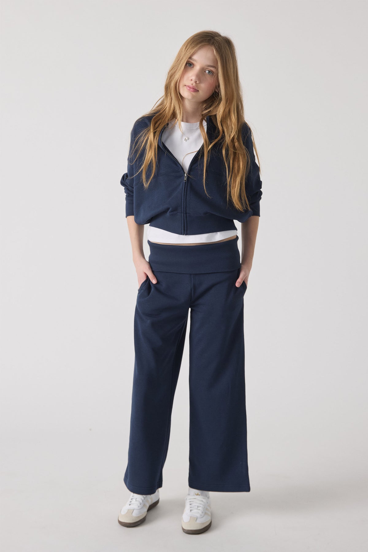 Girl wearing navy rolled waist track pants paired with a white tee and matching zip-up jacket and white sneakers