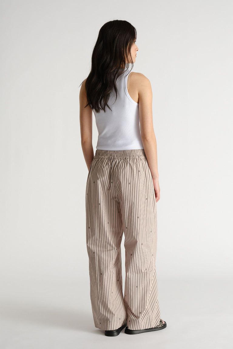 Woman wearing relaxed beige striped pants with a white sleeveless top, shown from behind for casual style