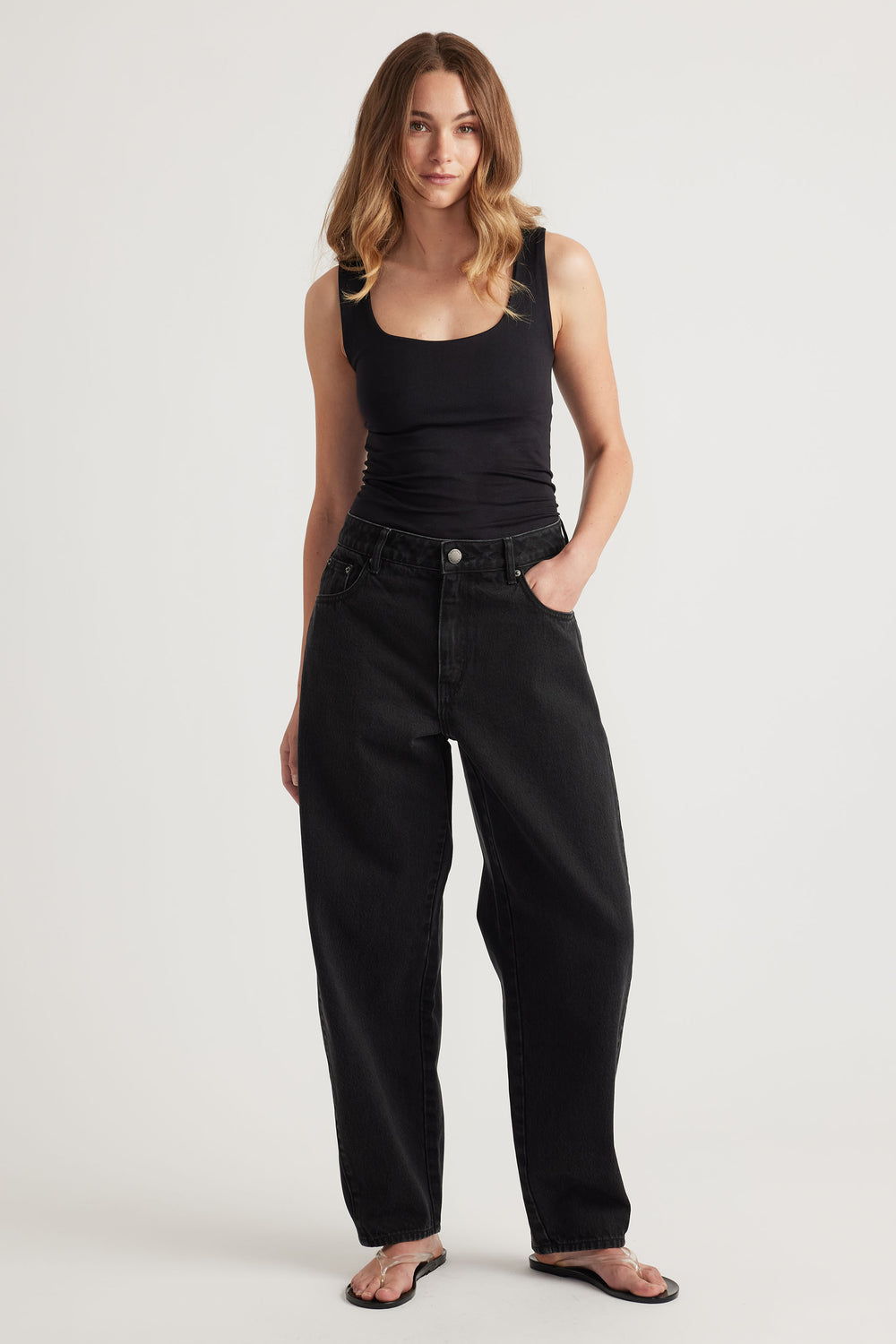 Woman wearing a fitted black scoop tank paired with relaxed high-rise black denim jeans and simple sandals