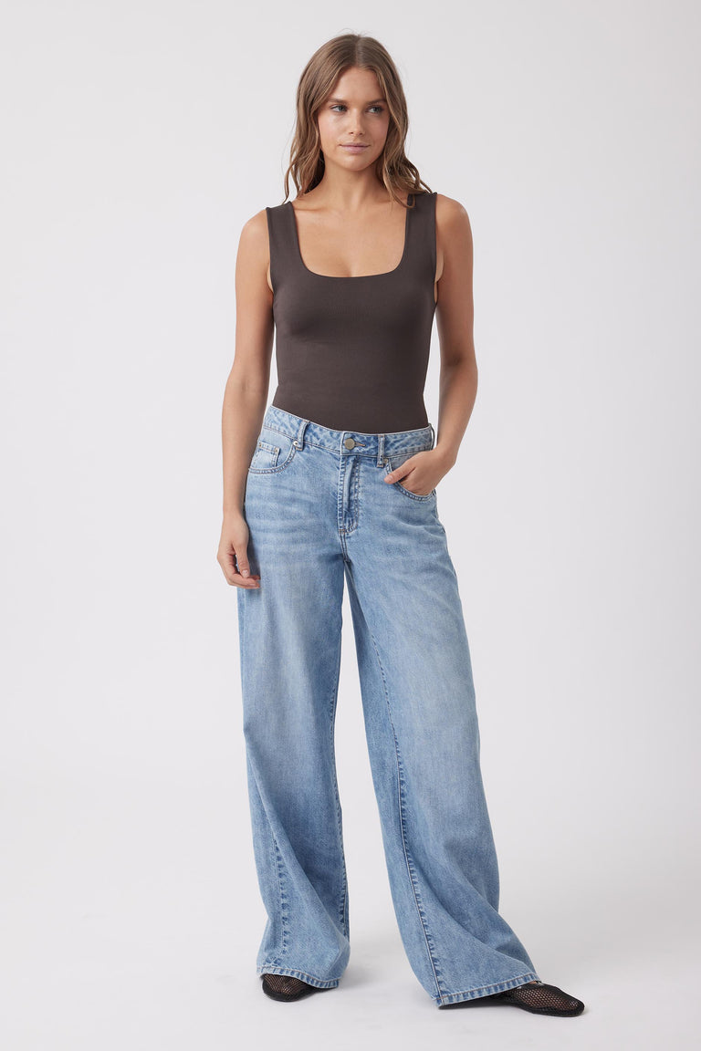 Model wearing a fitted brown sleeveless scoop neck tank top with wide leg blue jeans