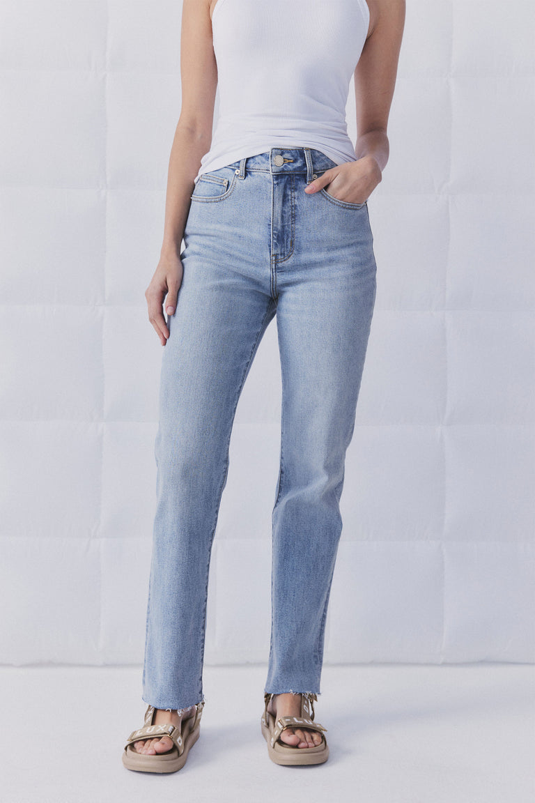 Woman wearing light blue straight leg jeans with a raw hem paired with a white sleeveless top and beige sandals