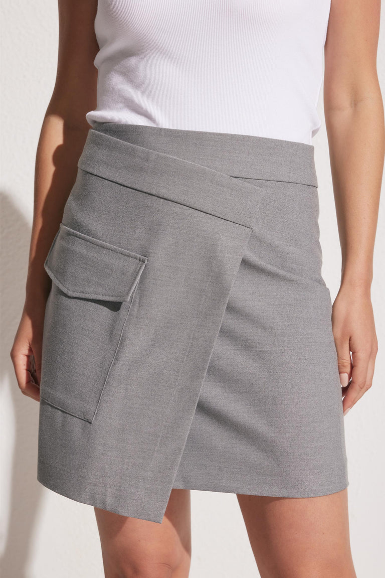 Woman wearing a grey asymmetric mini skirt with a front flap pocket paired with a white sleeveless top