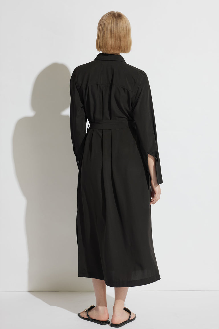 Woman wearing a black collared maxi dress with long sleeves and waist ties, viewed from behind