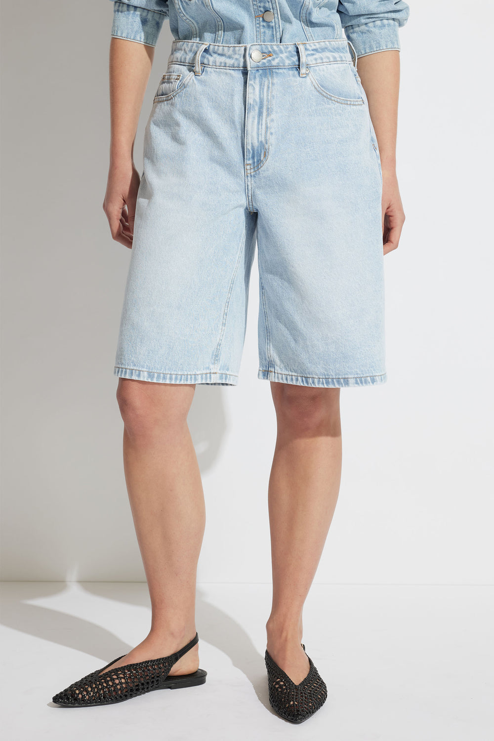 Light wash longline denim shorts styled with woven black flats, perfect for effortless casual summer looks.