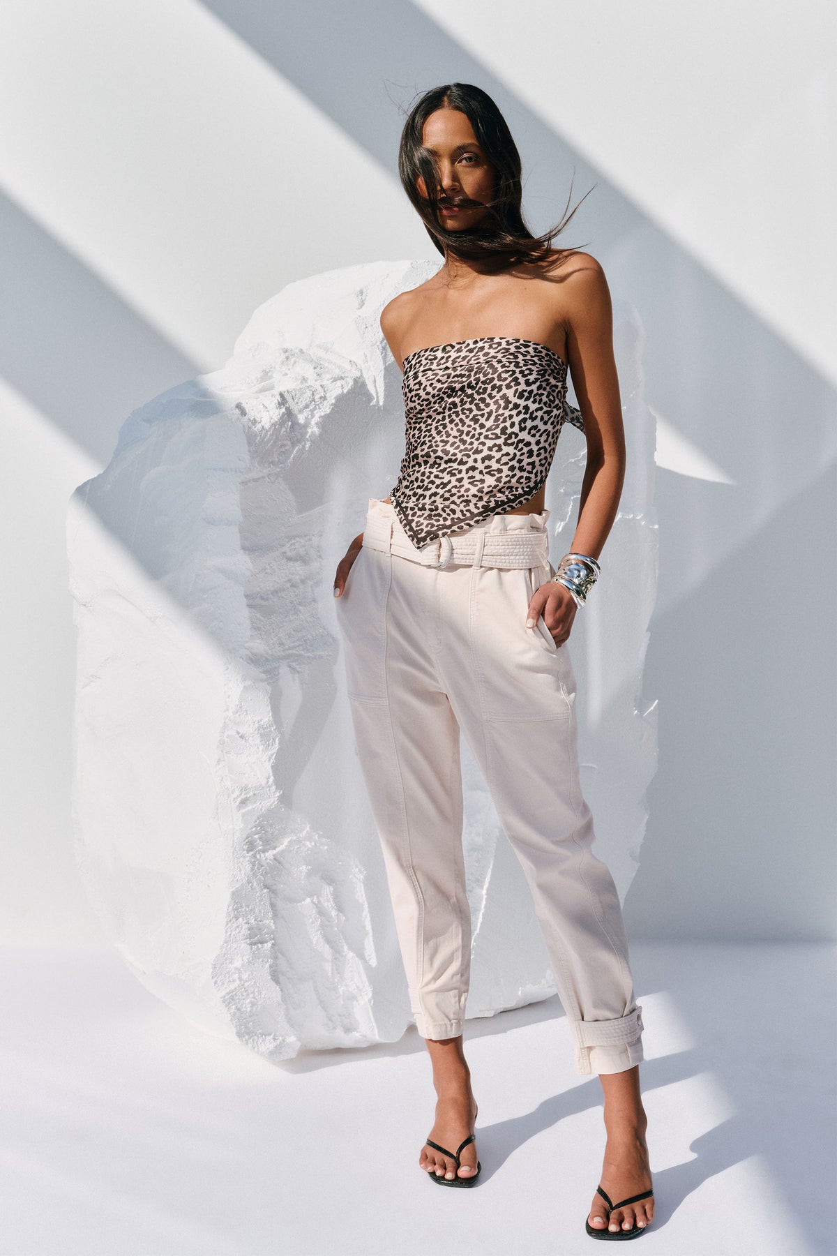 Woman wearing light stone-colored pull on pants with belt, paired with a leopard print strapless top and black sandals.