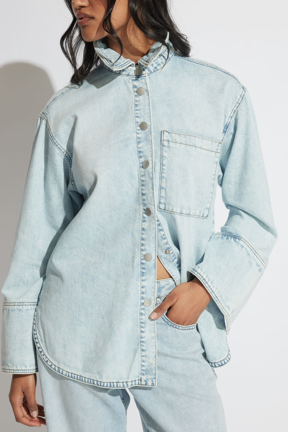 Woman wearing a light wash denim shirt with snap buttons and oversized cuffs paired with matching denim jeans