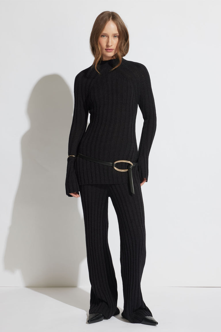 Woman wearing a fitted black rib knit sweater and matching rib knit pants styled with a slim belt and black shoes
