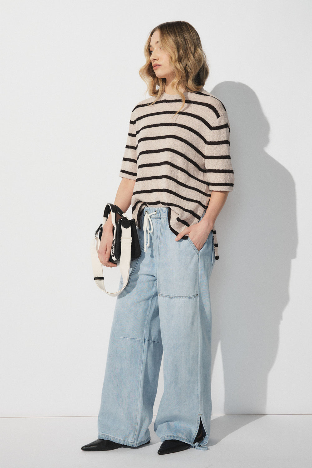 Woman wearing a beige and black striped short sleeve top with light blue wide-leg denim joggers and black boots