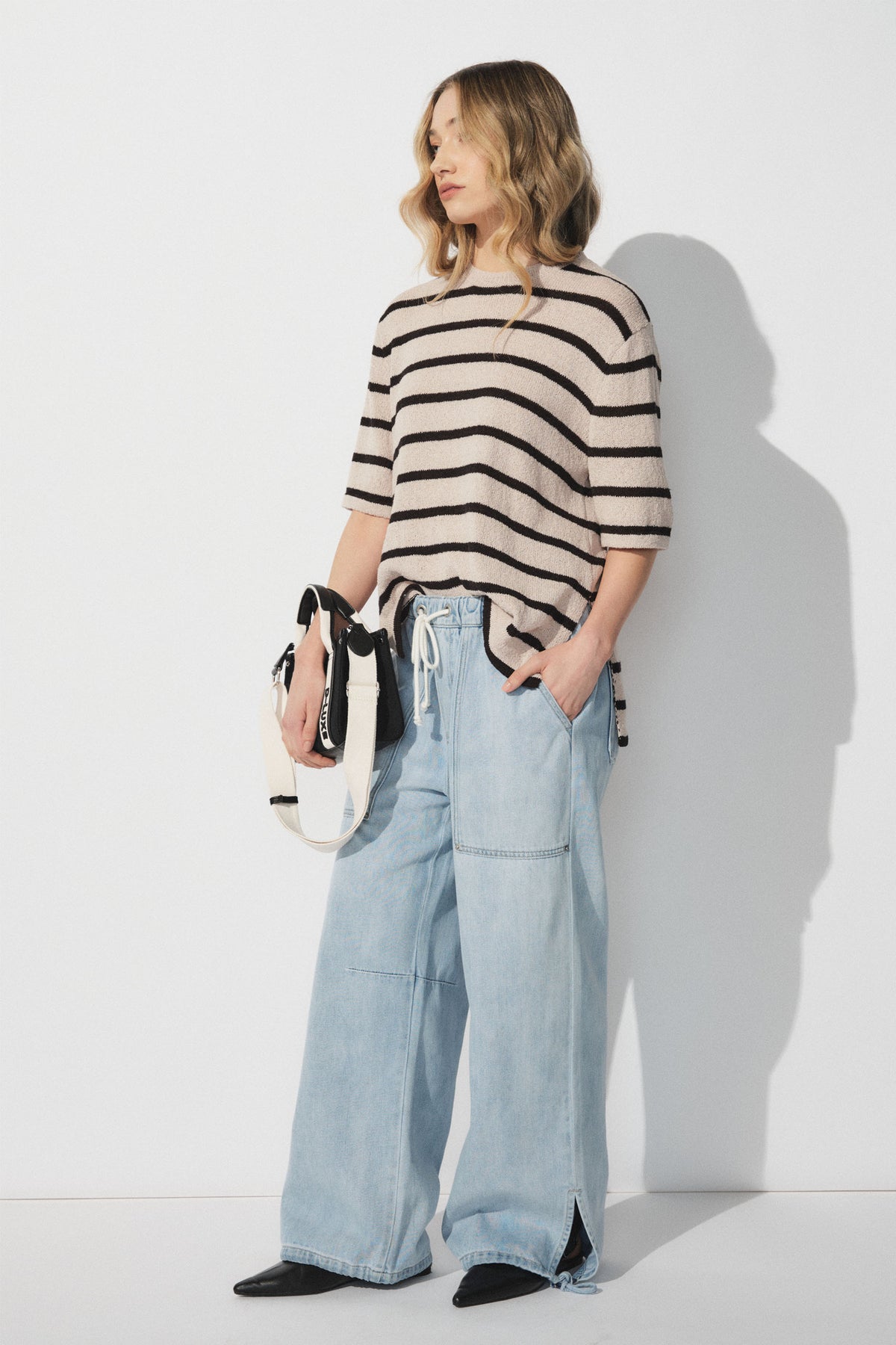 Woman wearing a beige and black striped short sleeve top with light blue wide-leg denim joggers and black boots