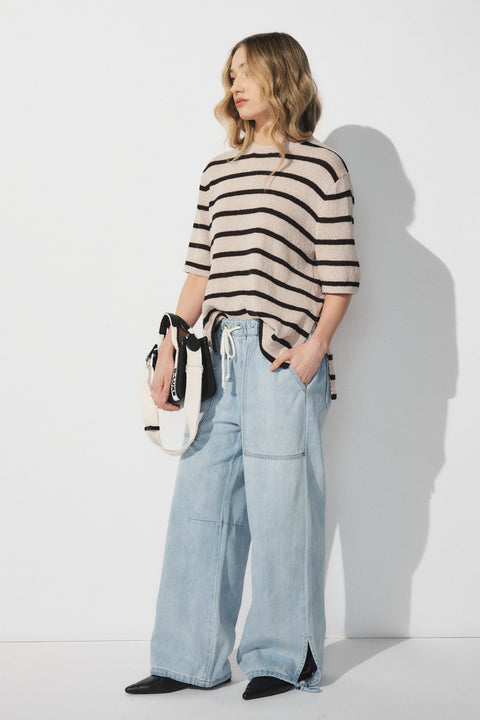 Woman wearing a beige and black striped short sleeve top with light blue wide-leg denim joggers and black boots