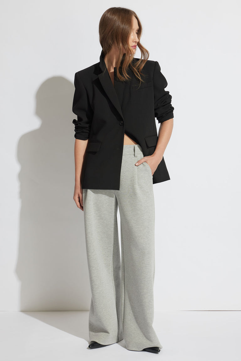 Woman wearing a relaxed grey belted pant paired with a black blazer, styled with minimal accessories and loose hair