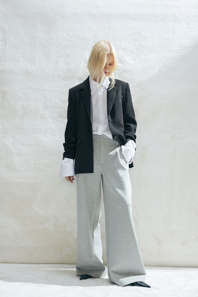 Woman wearing a white shirt with extended cuffs, a black blazer, and wide-leg light grey Nora Belted pull on pants