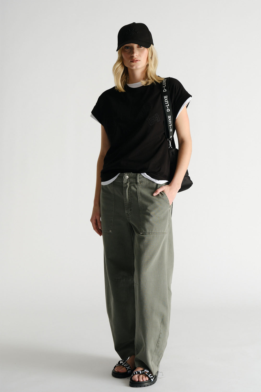 Woman wearing black D-Luxe Collegiate Tonal Tee with olive wide-leg pants and black cap by Decjuba Australian brand