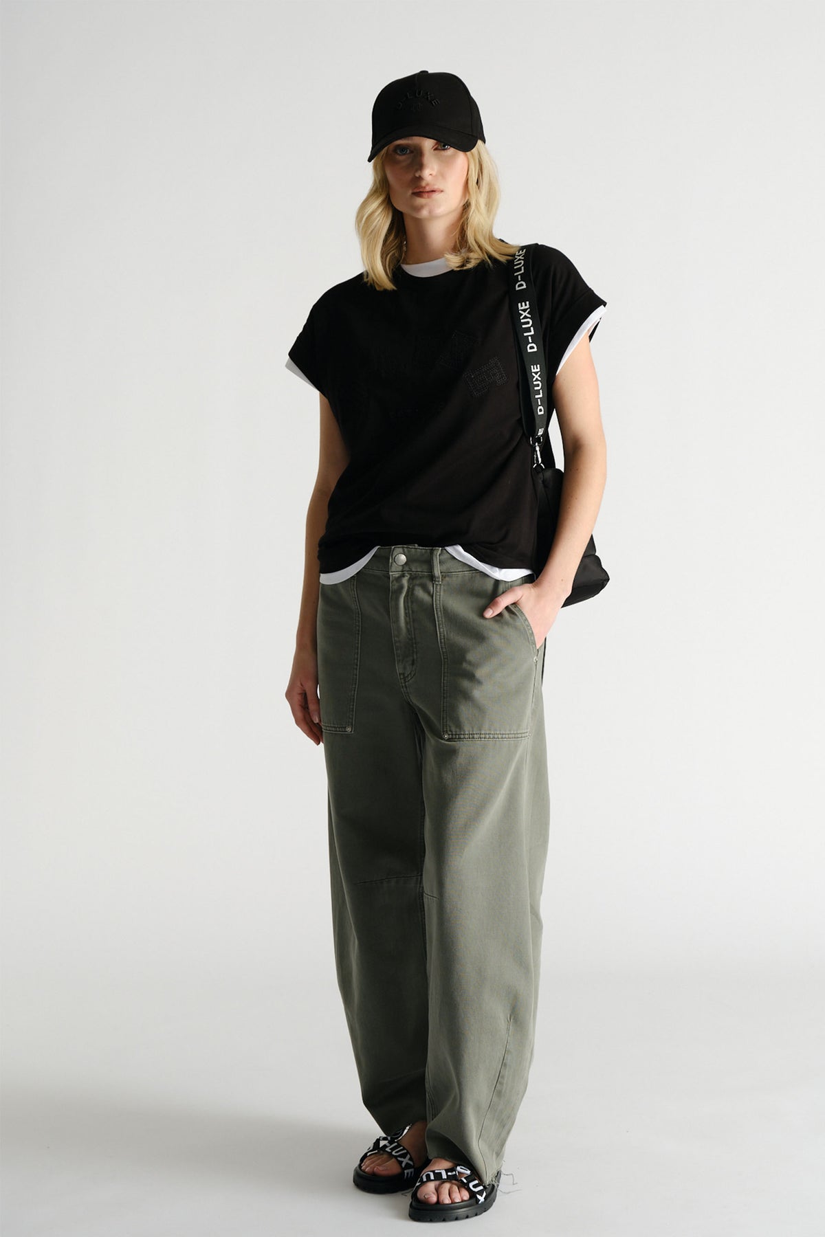 Woman wearing black D-Luxe Collegiate Tonal Tee with olive wide-leg pants and black cap by Decjuba Australian brand