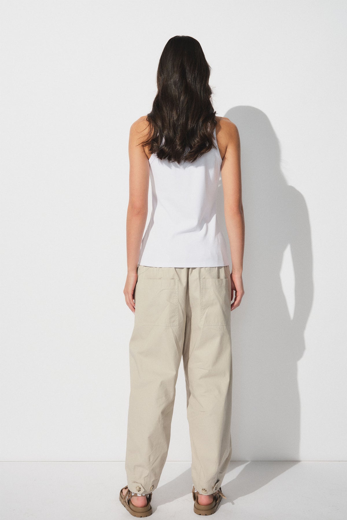 Back view of woman wearing a white ribbed tank top paired with relaxed beige cargo pants and casual sandals