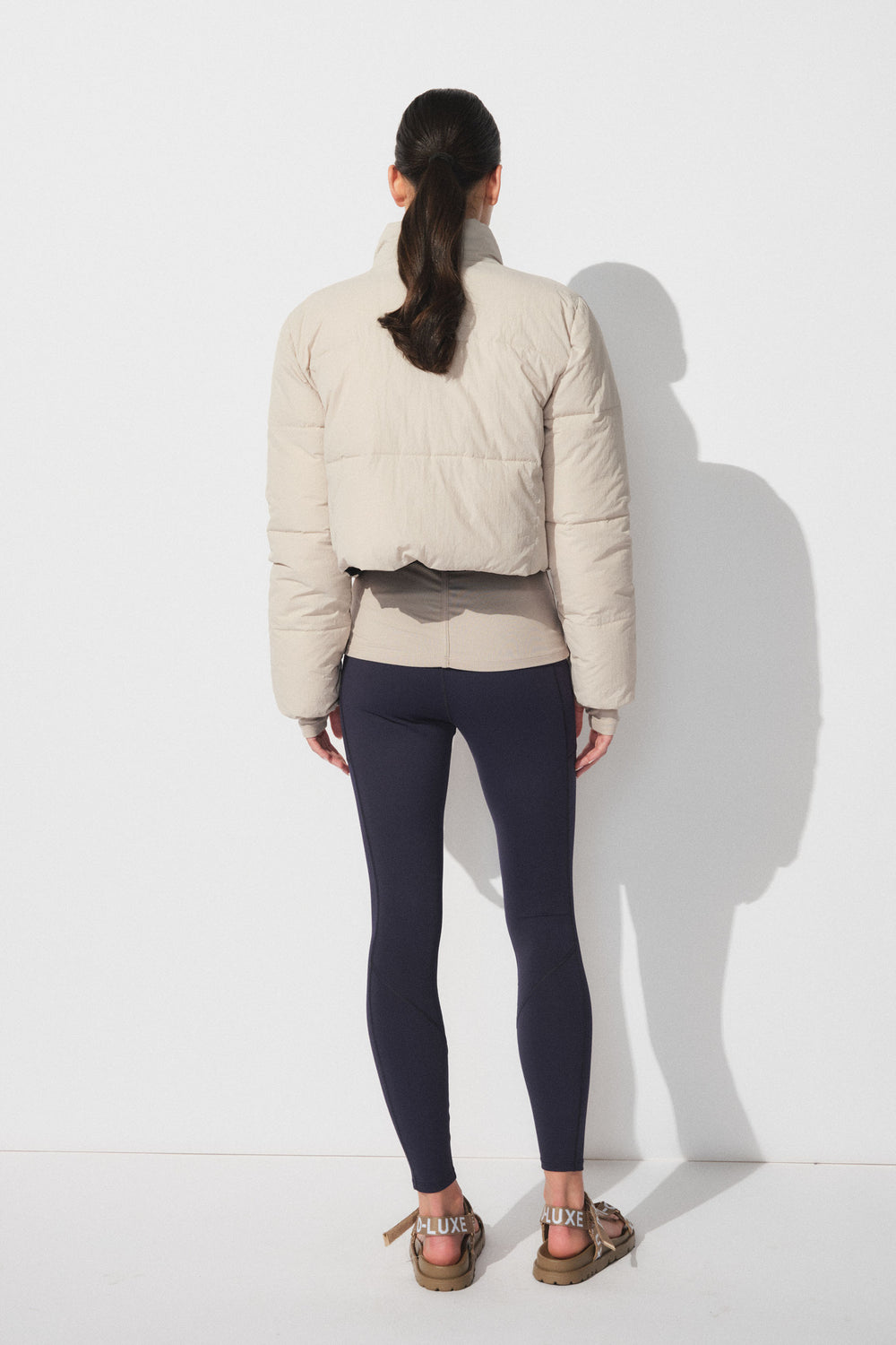 Back view of woman wearing navy fitted leggings paired with a cropped beige puffer jacket and casual sandals.