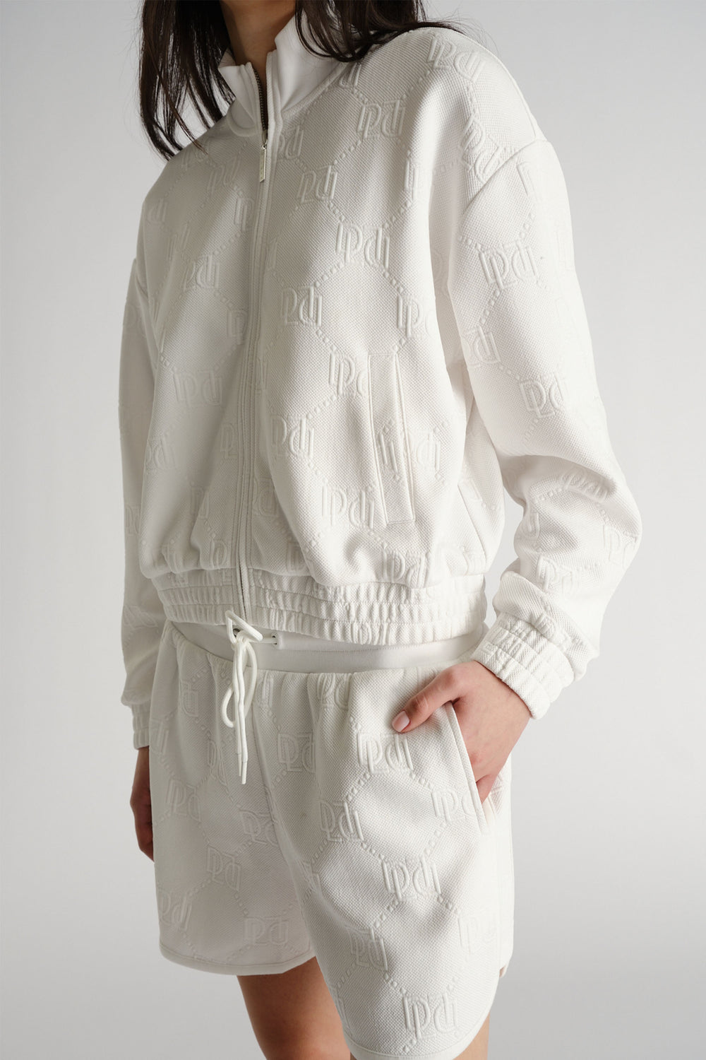 Woman wearing an embossed white zip-up sweatshirt and matching relaxed-fit sweat shorts with side pockets