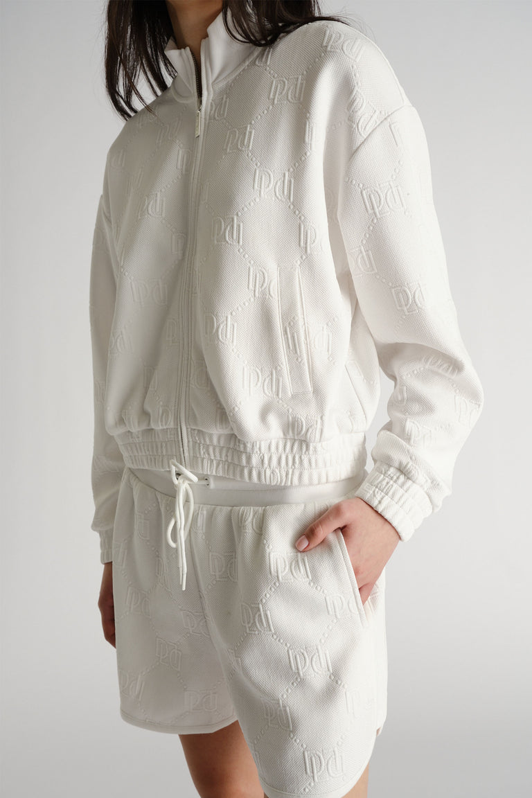 Woman wearing an embossed white zip-up sweatshirt and matching relaxed-fit sweat shorts with side pockets