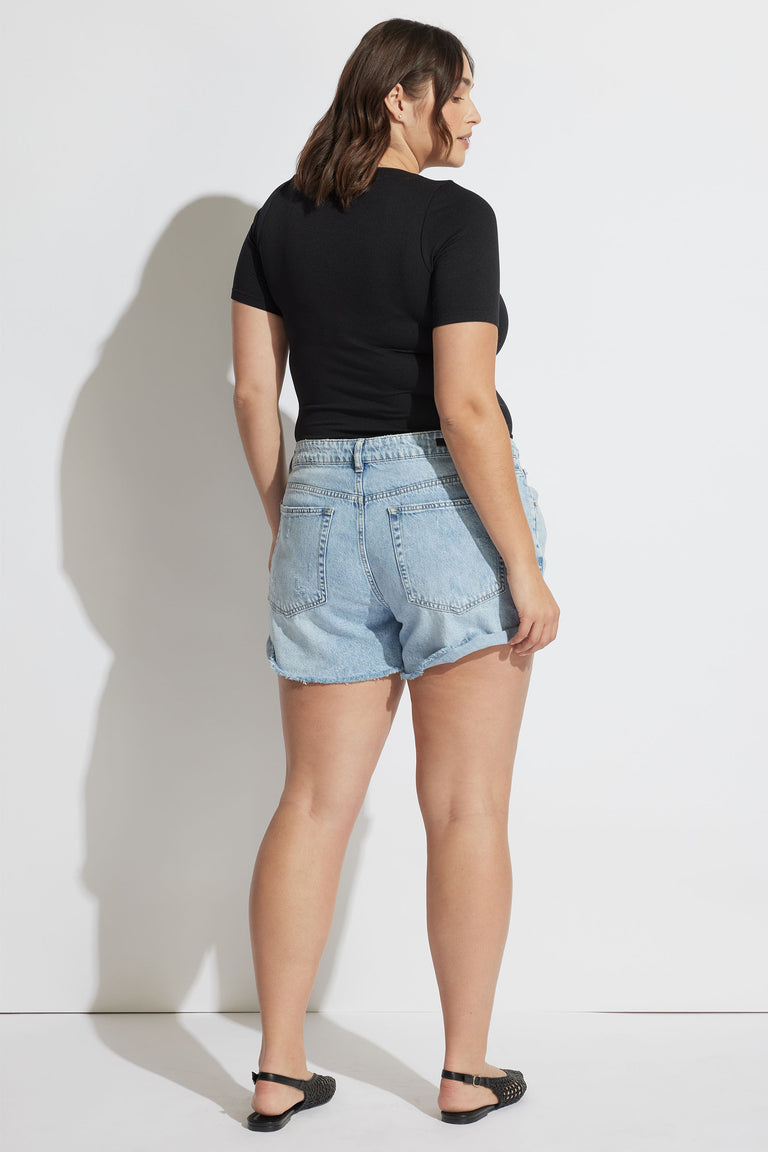 Woman wearing light blue rolled cuff denim shorts paired with a fitted black short sleeve top and black flats