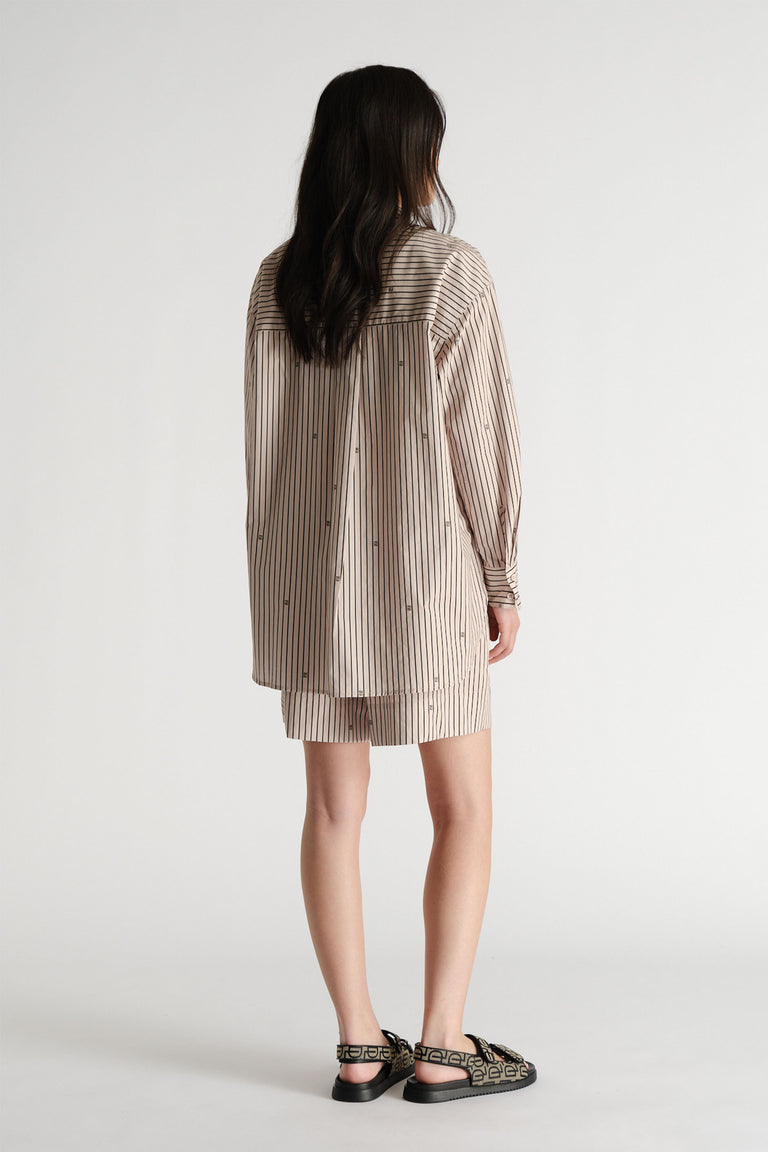 Woman wearing an oversized striped shirt layered over matching shorts with patterned sandals in a minimalist setting