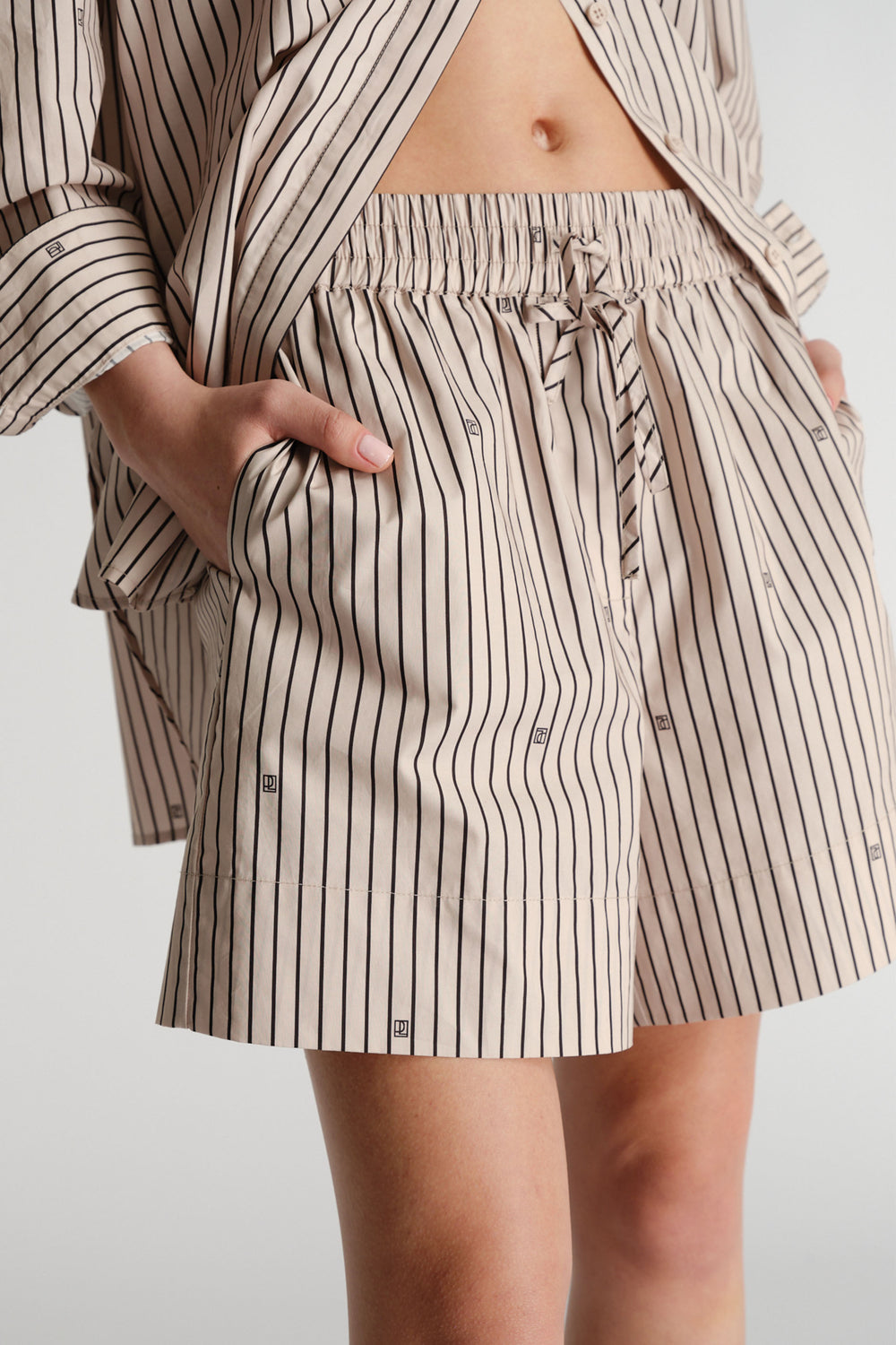 Close-up of woman wearing beige striped shorts with elastic waist and subtle monogram print, paired with matching shirt.
