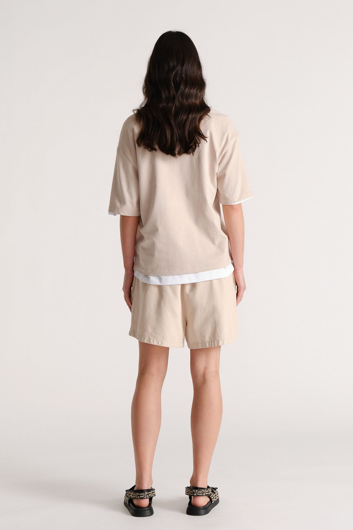 Model wearing a relaxed beige top and matching elastic waist shorts viewed from behind