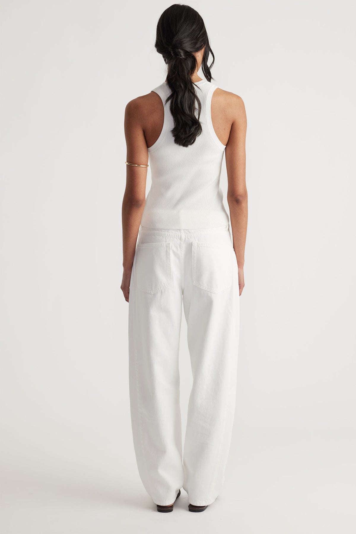 Back view of a woman wearing an ivory racer back knit tank paired with relaxed white wide-leg pants.