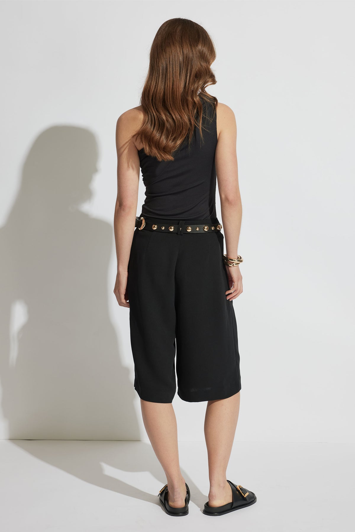 Woman seen from behind wearing a black one-shoulder top paired with cropped wide-leg black pants and slip-on shoes