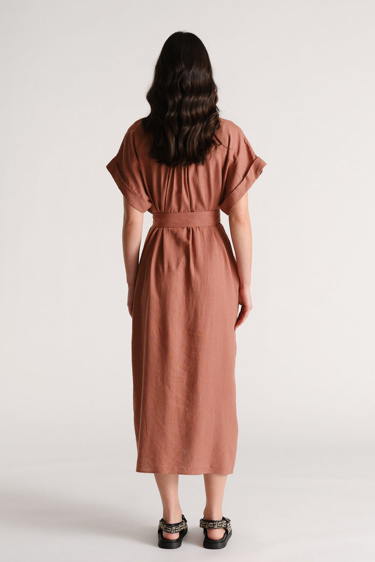 Woman seen from behind wearing a rust-colored linen blend midi dress with cuffed sleeves and a wide belt at the waist